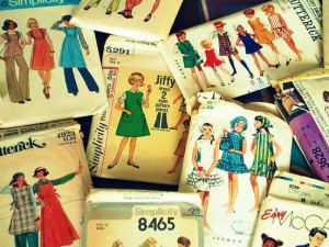 Several old dress pattern packets scattered over a surface. The dresses on the packet covers are colourful.